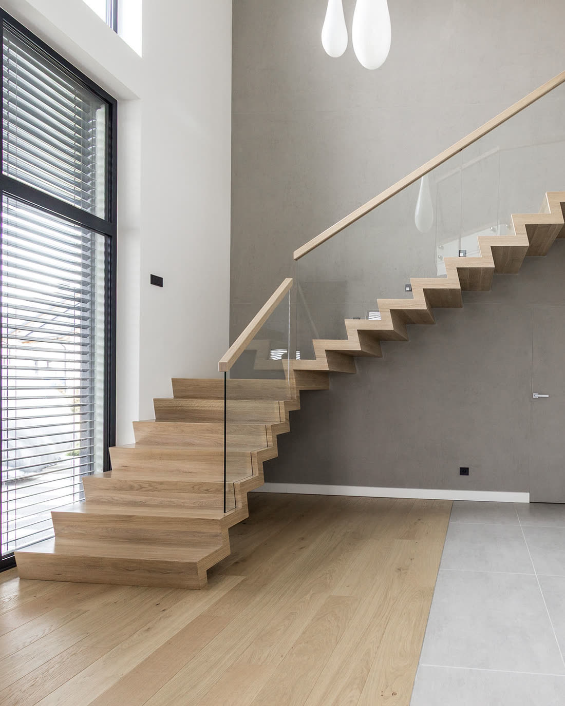 Jasne dębowe schody ze szklaną balustradą przy oknie